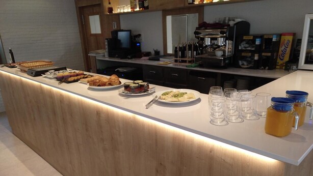 A breakfast bar with various food items and drinks, a coffee machine, and a television in the background. - Hotel Entrerailes (Casalarreina)