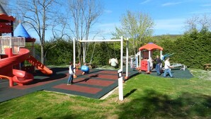 A playground with a red slide, swings, and a climbing structure. - Camping Les Tilleuls - Chalets (Rocamadour)