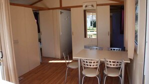 A room with a wooden floor, a table with four chairs, and a window. - Camping Les Tilleuls - Chalets (Rocamadour)