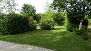 A well-maintained grassy area with dense hedges and trees, a gravel path, and a clear sky. - Camping Les Tilleuls - Chalets (Rocamadour)