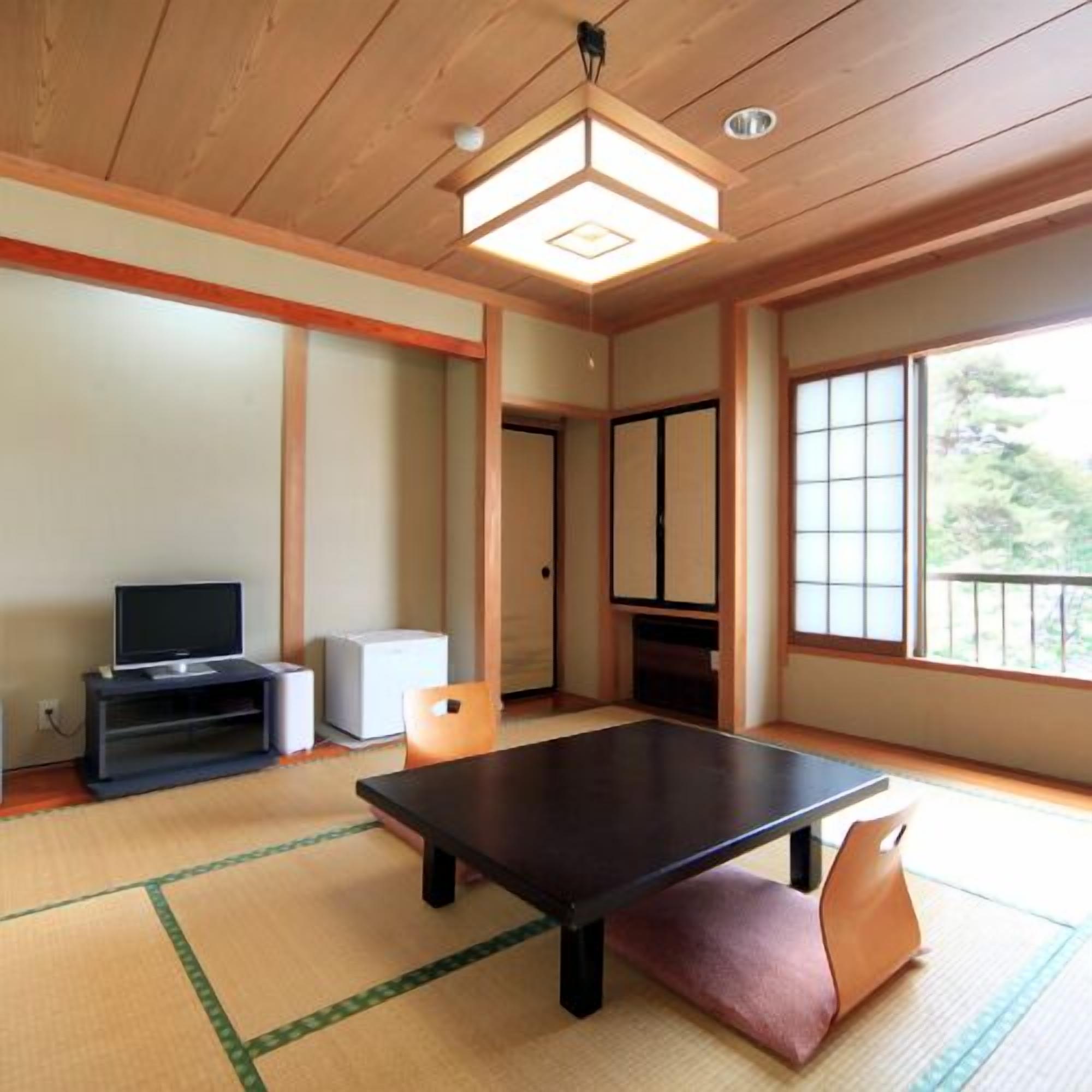 A traditional Japanese room with tatami flooring, a low table, a television on a stand, and sliding doors.