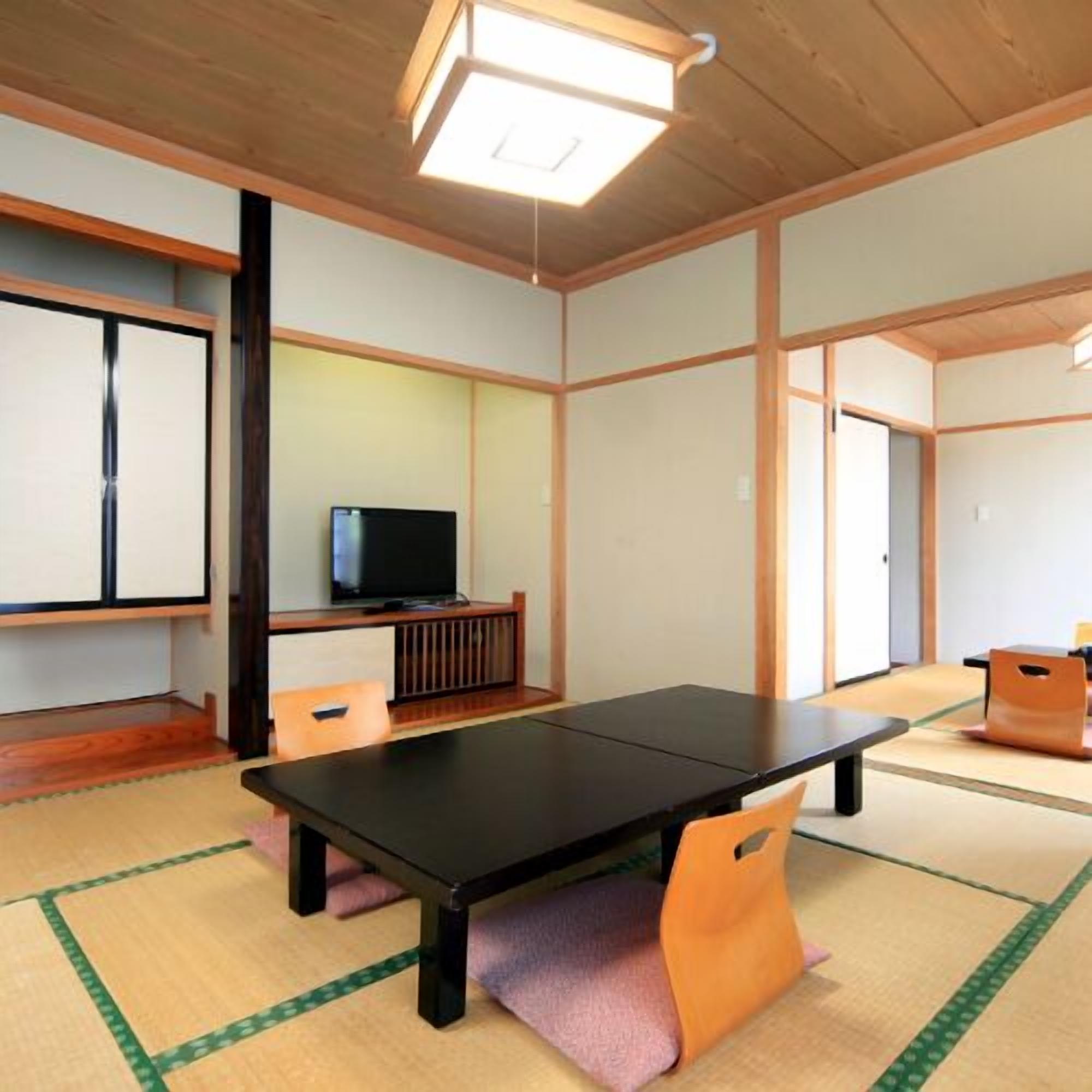 A tatami mat room with a black table, chairs, a television, and sliding doors.