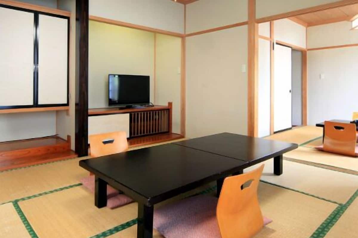 Una habitación con esteras de tatami, una mesa negra, sillas, un televisor y puertas correderas.