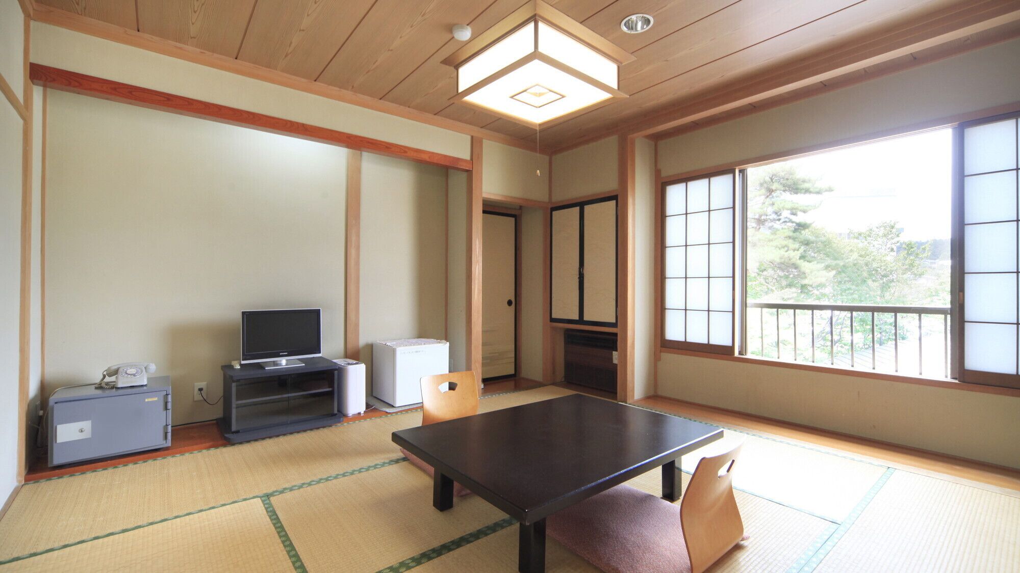 A traditional Japanese room with tatami flooring, a low table, a television, and a cabinet.