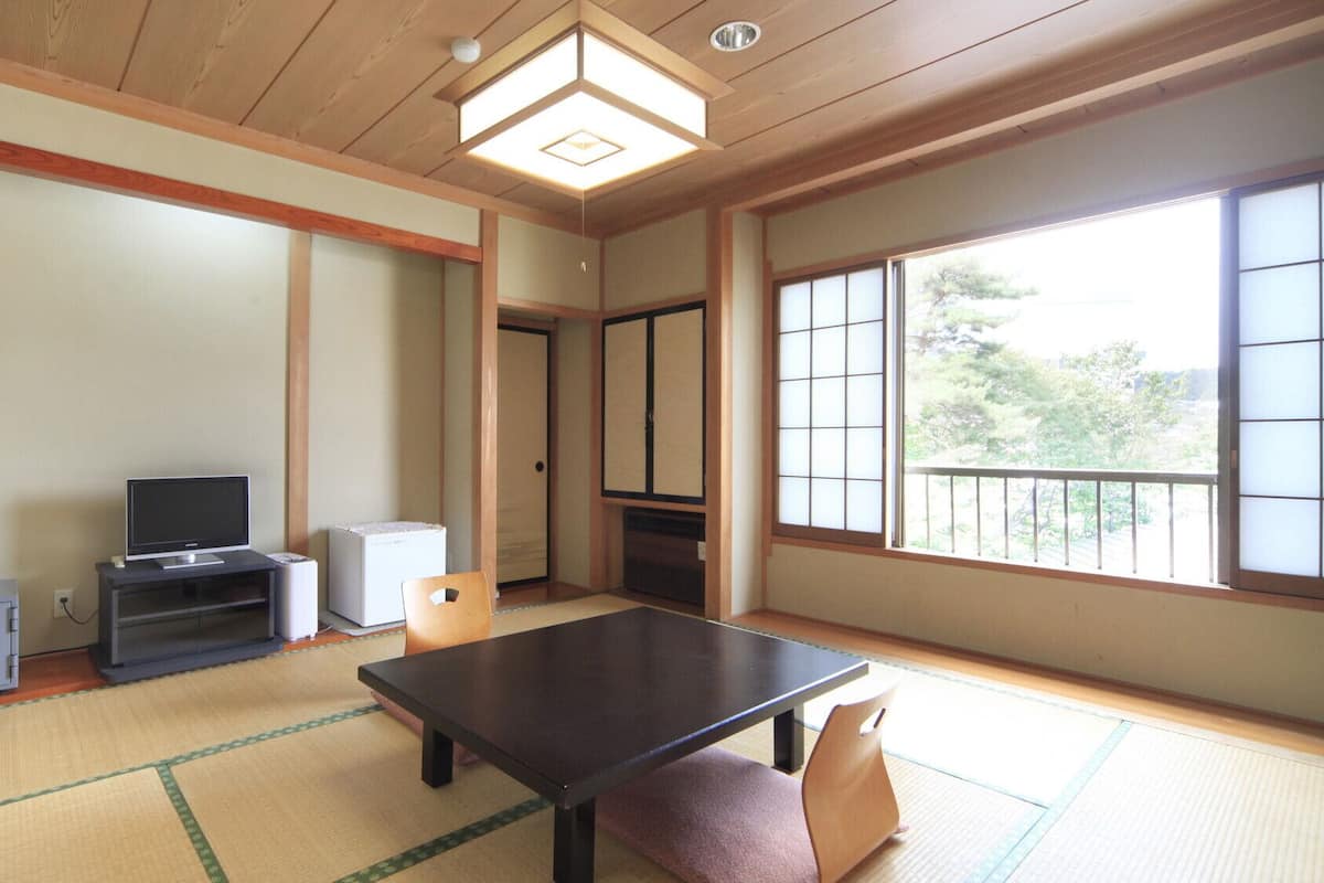 Una habitación japonesa tradicional con suelo de tatami, una mesa baja, un televisor y un armario.