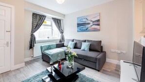 A modern living room with a grey sofa, a coffee table, and a painting of a mountain landscape. - HiikotsHomes - Dartford (Dartford)