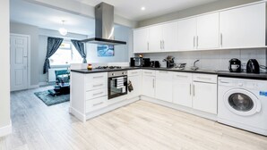A modern kitchen with white cabinets, a built-in oven, a washing machine, and a gas stove. - HiikotsHomes - Dartford (Dartford)