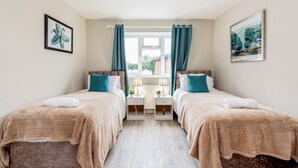 A bedroom with two beds, a window with curtains, bedside tables with lamps, and artwork on the walls. - HiikotsHomes - Dartford (Dartford)