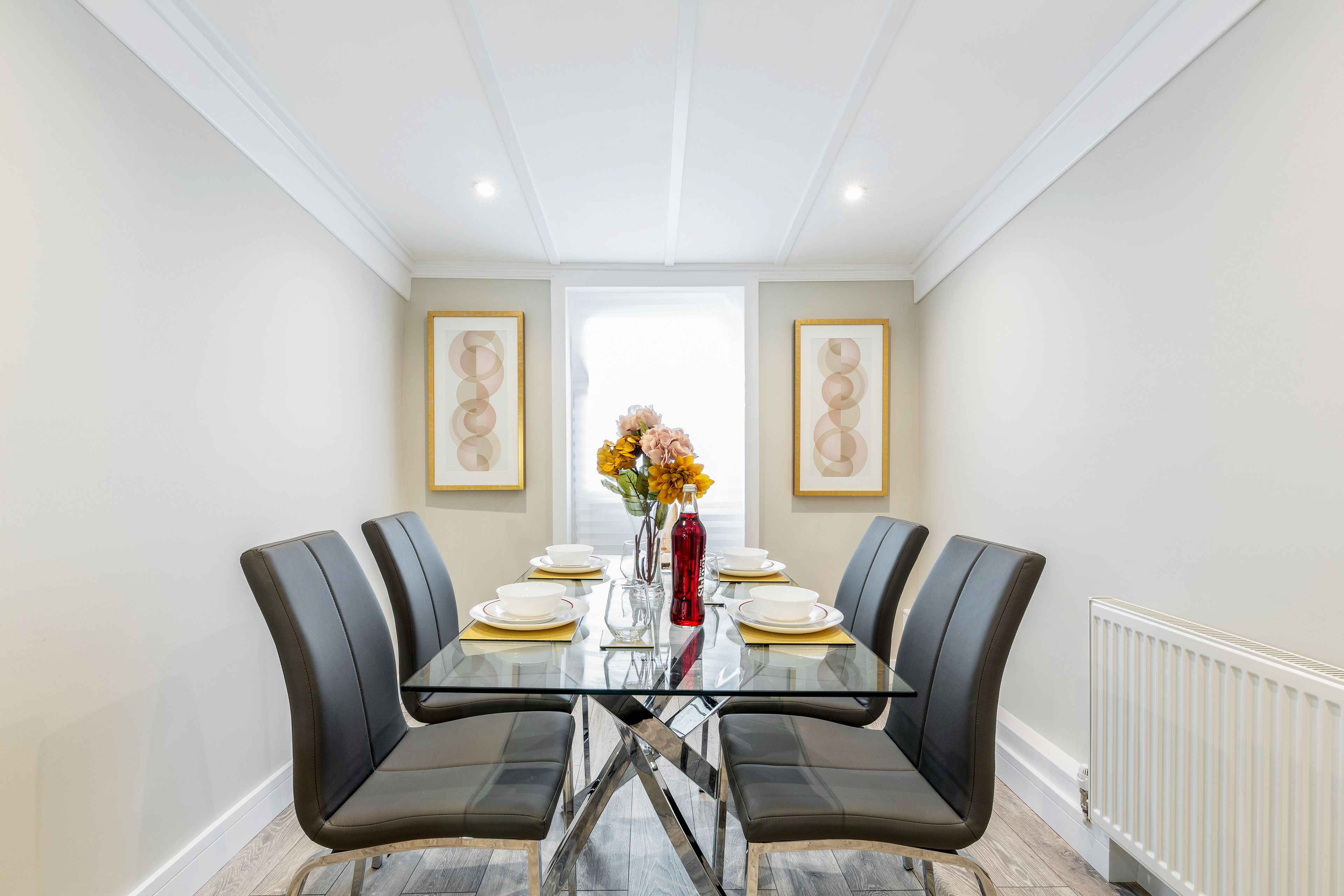 En spisestue med et glastop bord, sorte stole og en vase med blomster.