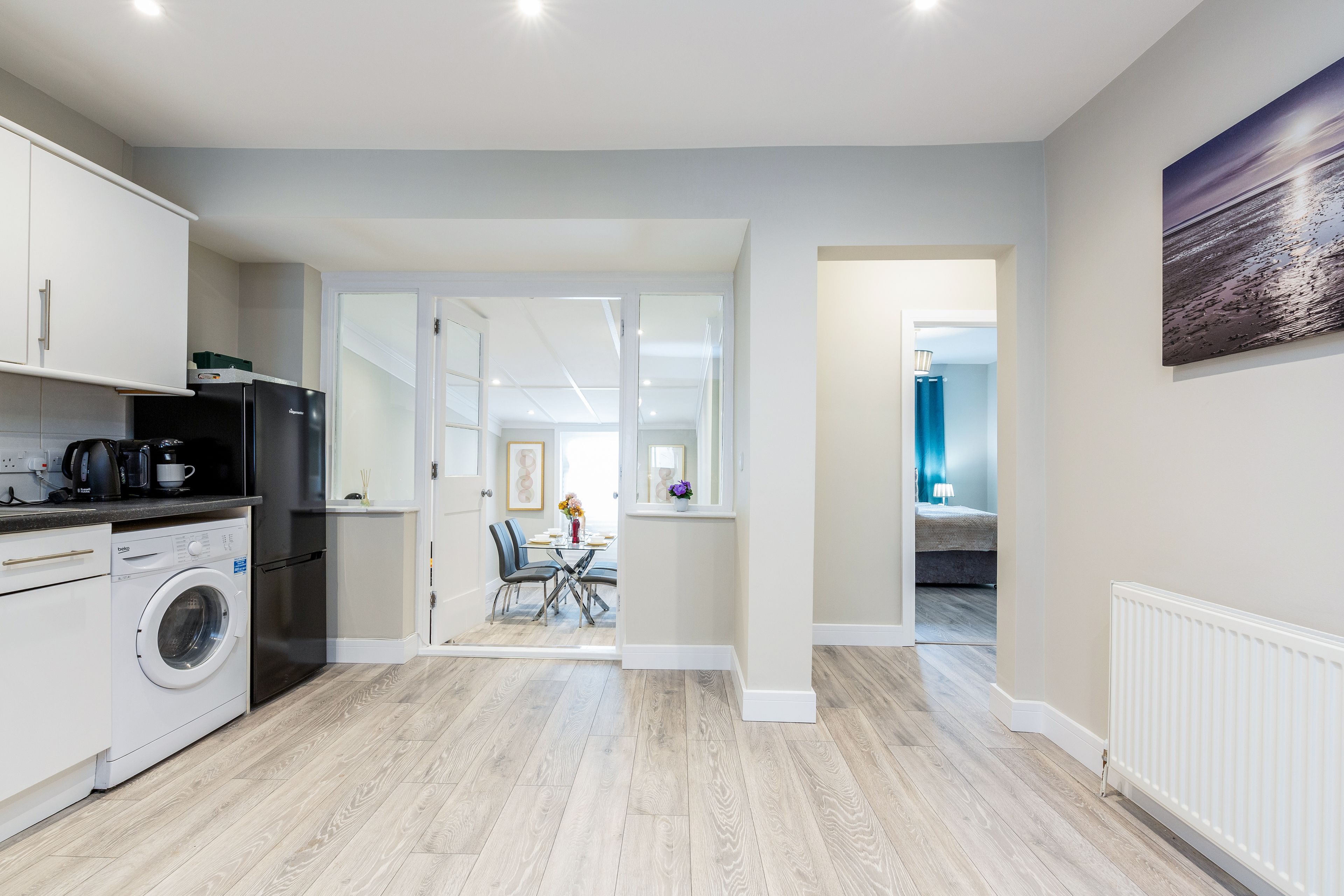 A modern kitchen with a washing machine, a refrigerator, and a dining area with a table and chairs.