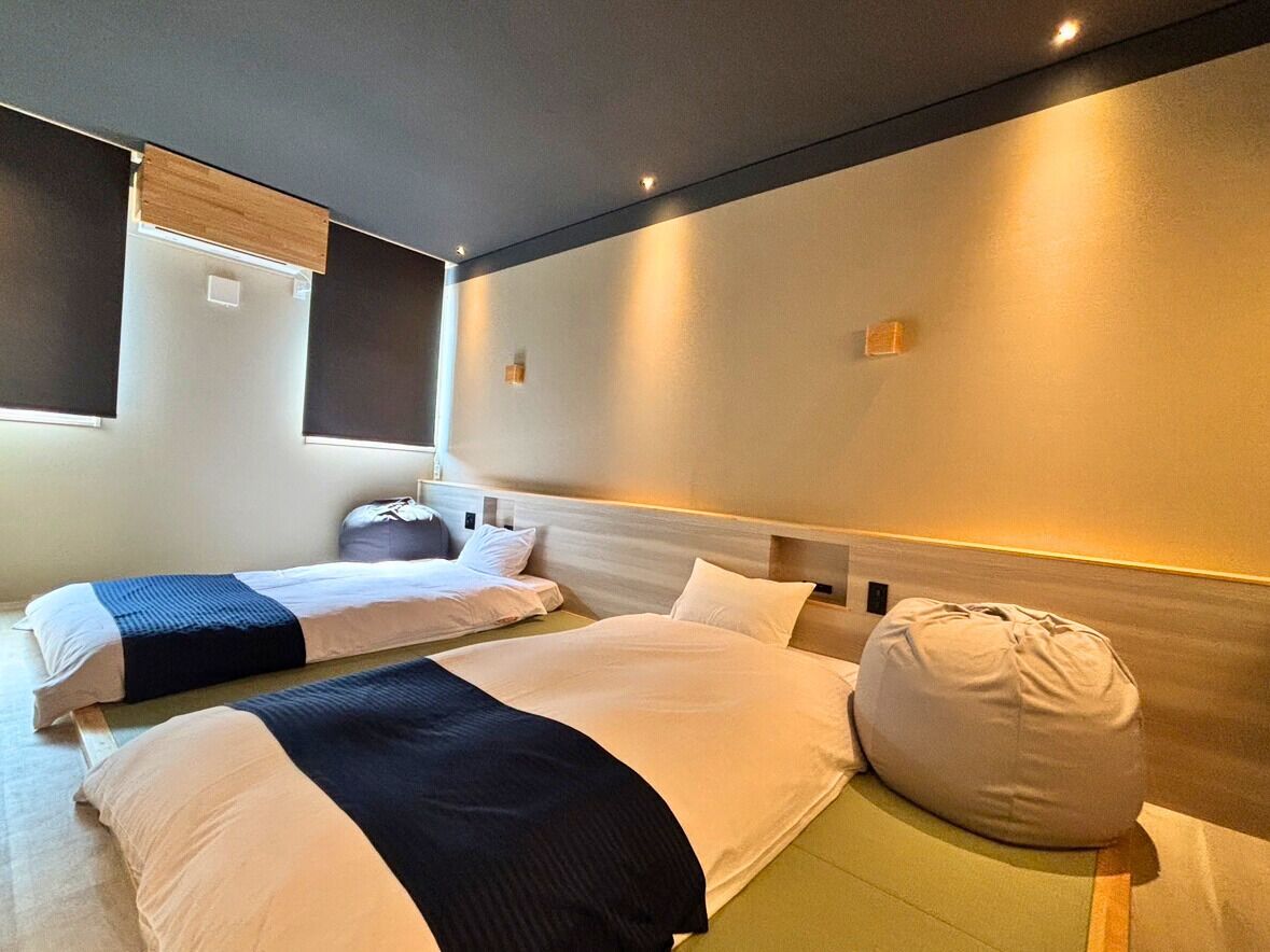 A hotel room with two beds, a bean bag chair, and a headboard with built-in lighting.