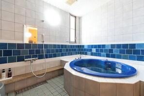 A bathroom with a blue jacuzzi tub, a shower area, and a window.