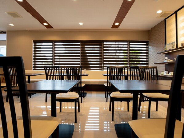 A modern dining area with wooden tables and chairs, large windows with blinds, and a clean, polished floor.