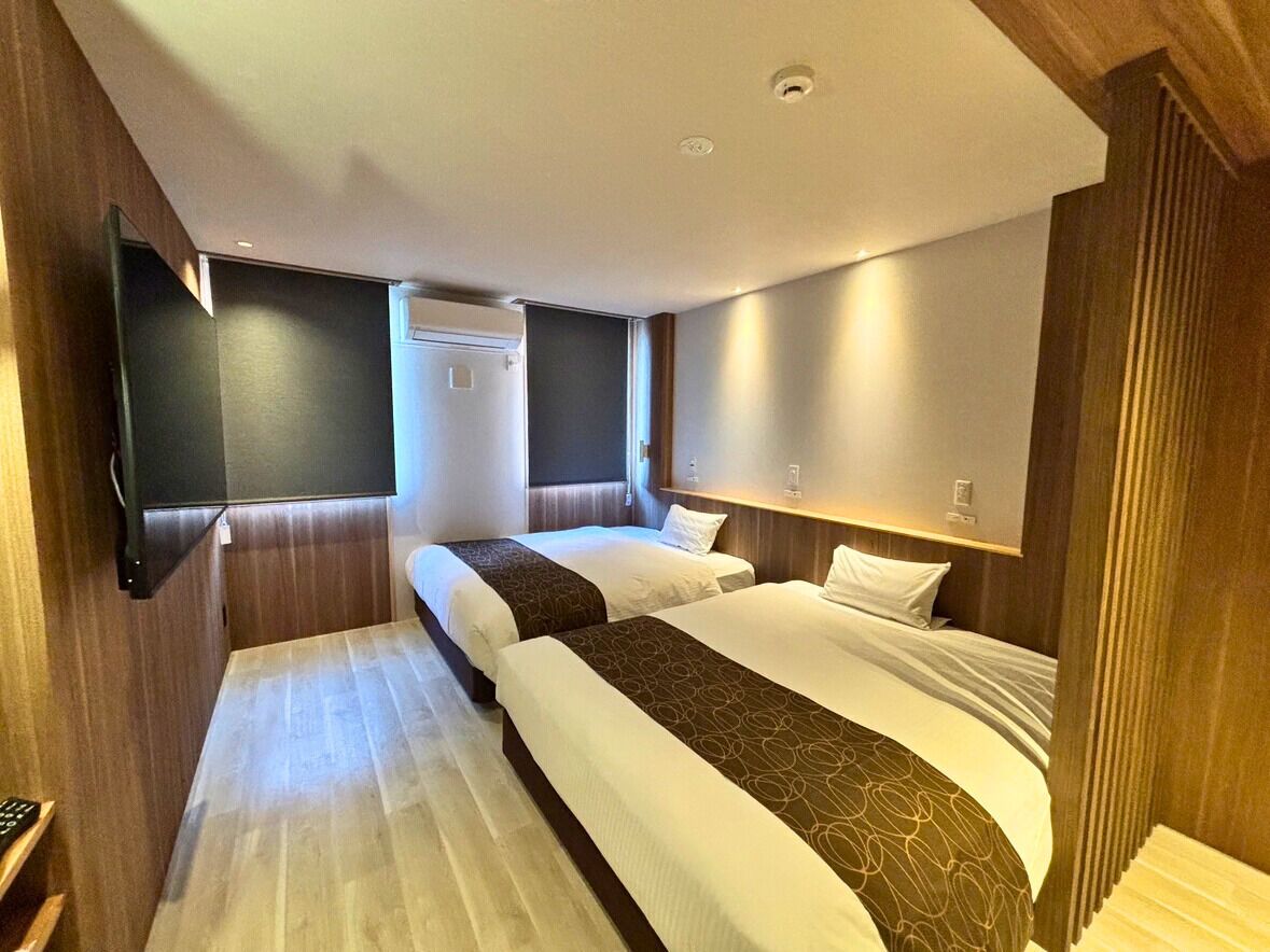A hotel room with two beds, a flat-screen TV mounted on the wall, and a wooden panel design.