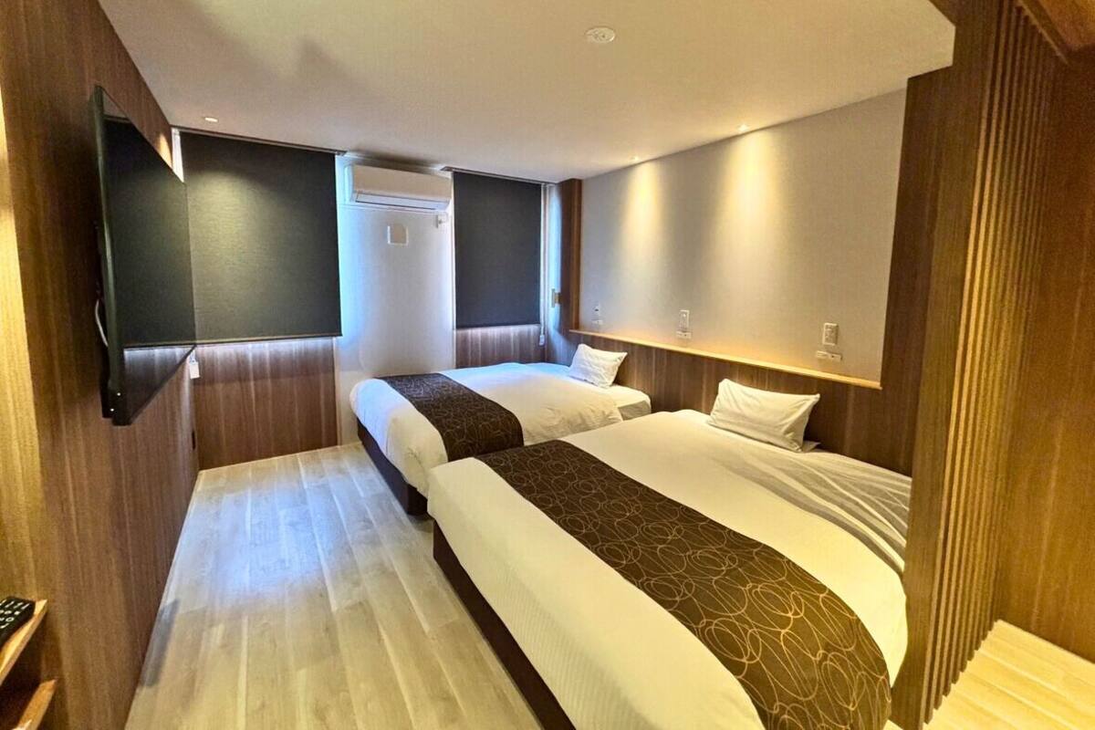 Ein Hotelzimmer mit zwei Betten, einem an der Wand montierten Flachbildfernseher und einer Holzpaneel-Wandgestaltung.