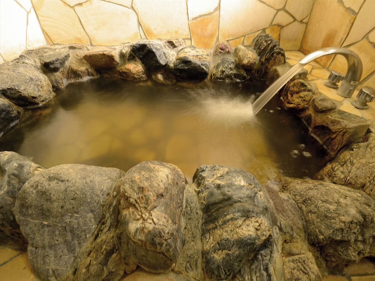 A stone hot tub with a faucet and a stone wall surrounding it.