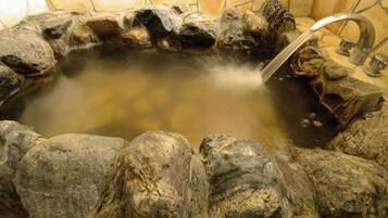 A stone hot tub with a faucet and a stone wall surrounding it.