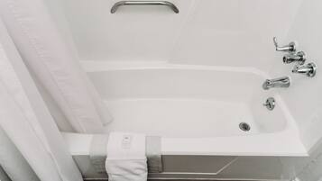Una bañera blanca con cortina de ducha, una toalla y un asidero.
