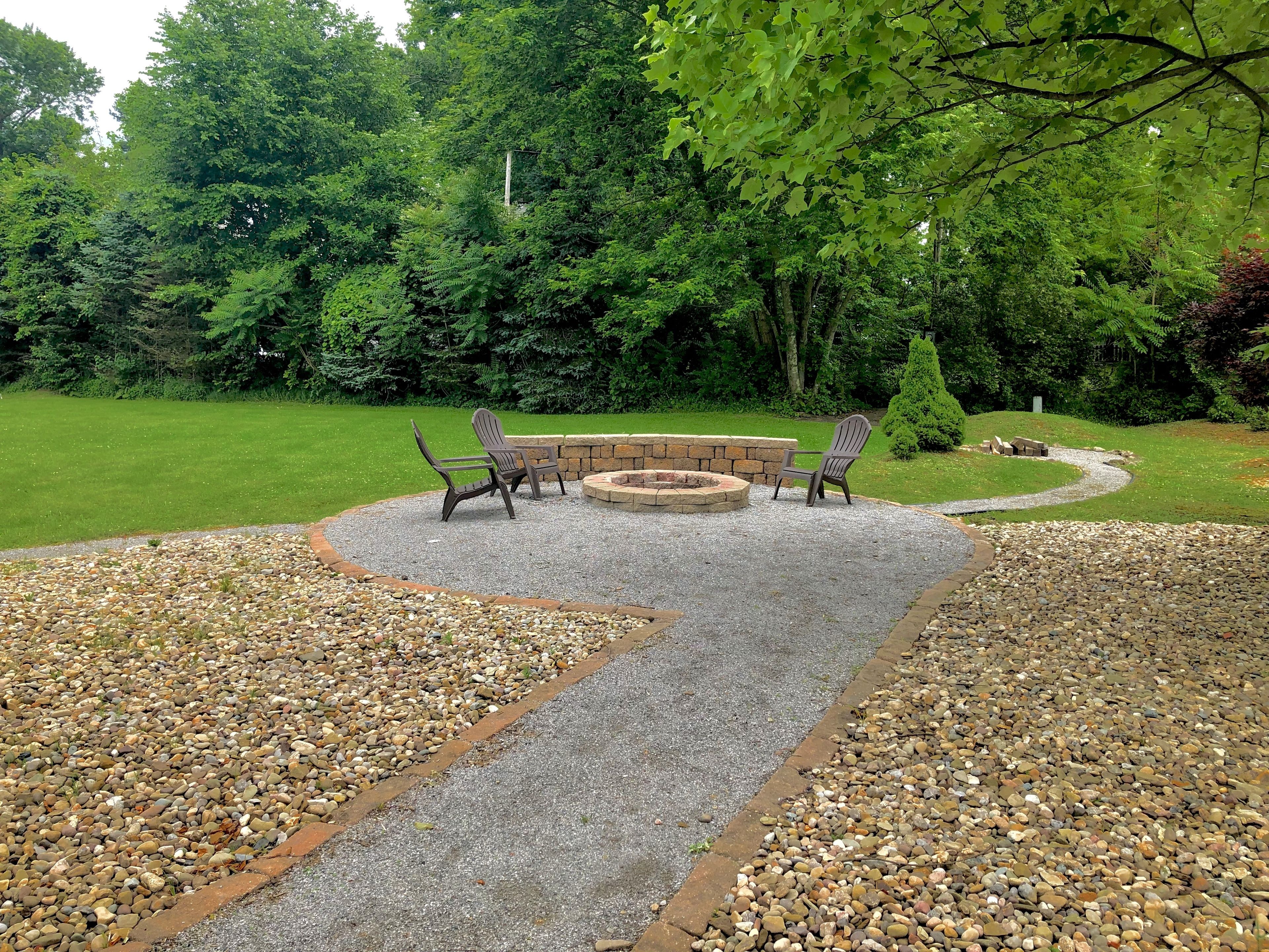 A patio area with a fire pit, two Adirondack chairs, and a stone wall.
