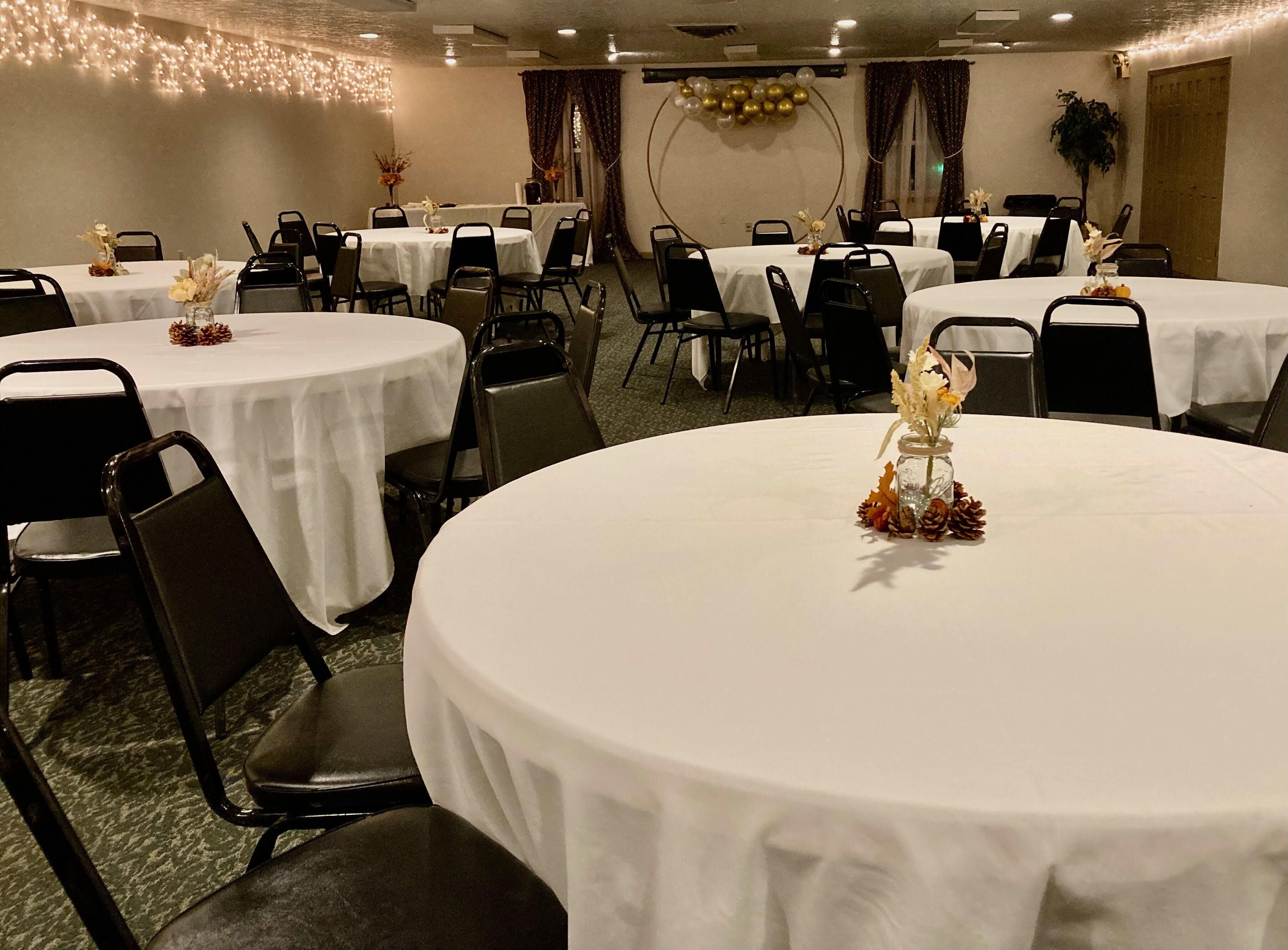 A hotel dining area with round tables, black chairs, and white tablecloths.