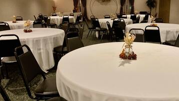 A hotel dining area with round tables, black chairs, and white tablecloths.