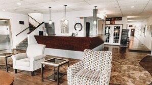 Un espace d’accueil comprenant un comptoir de réception en bois, un fauteuil blanc, un fauteuil à motifs et une table avec un plateau en verre.