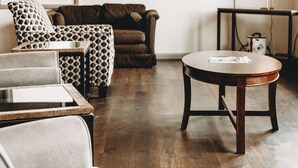 Un salon moderne avec un canapé, un fauteuil et une petite table. Un téléviseur est fixé au mur, et une fenêtre laisse entrer la lumière naturelle.