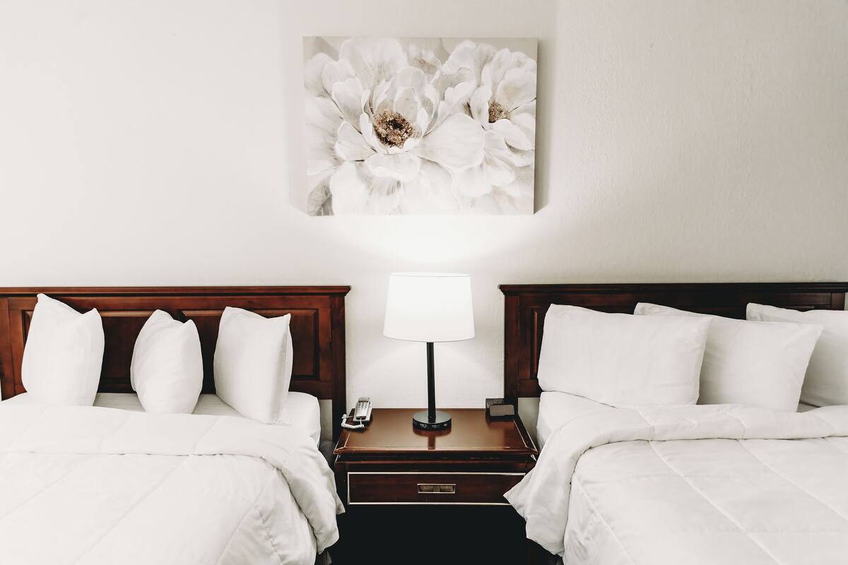 Une chambre d’hôtel avec deux lits, une table de chevet avec une lampe et une œuvre d’art florale accrochée au mur.