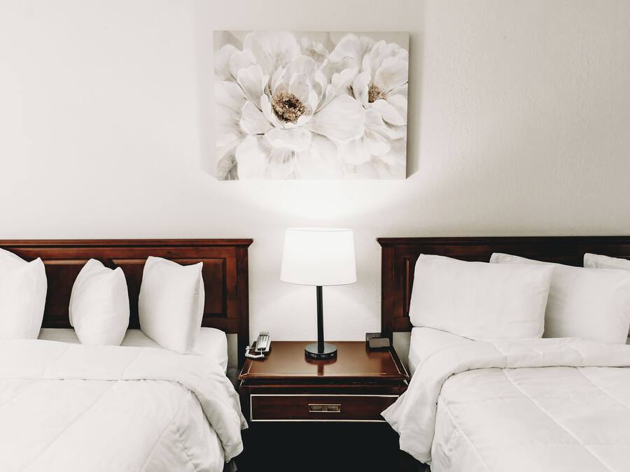 Ein Hotelzimmer mit zwei Betten, einem Nachttisch mit Lampe und einem Blumenbild an der Wand.