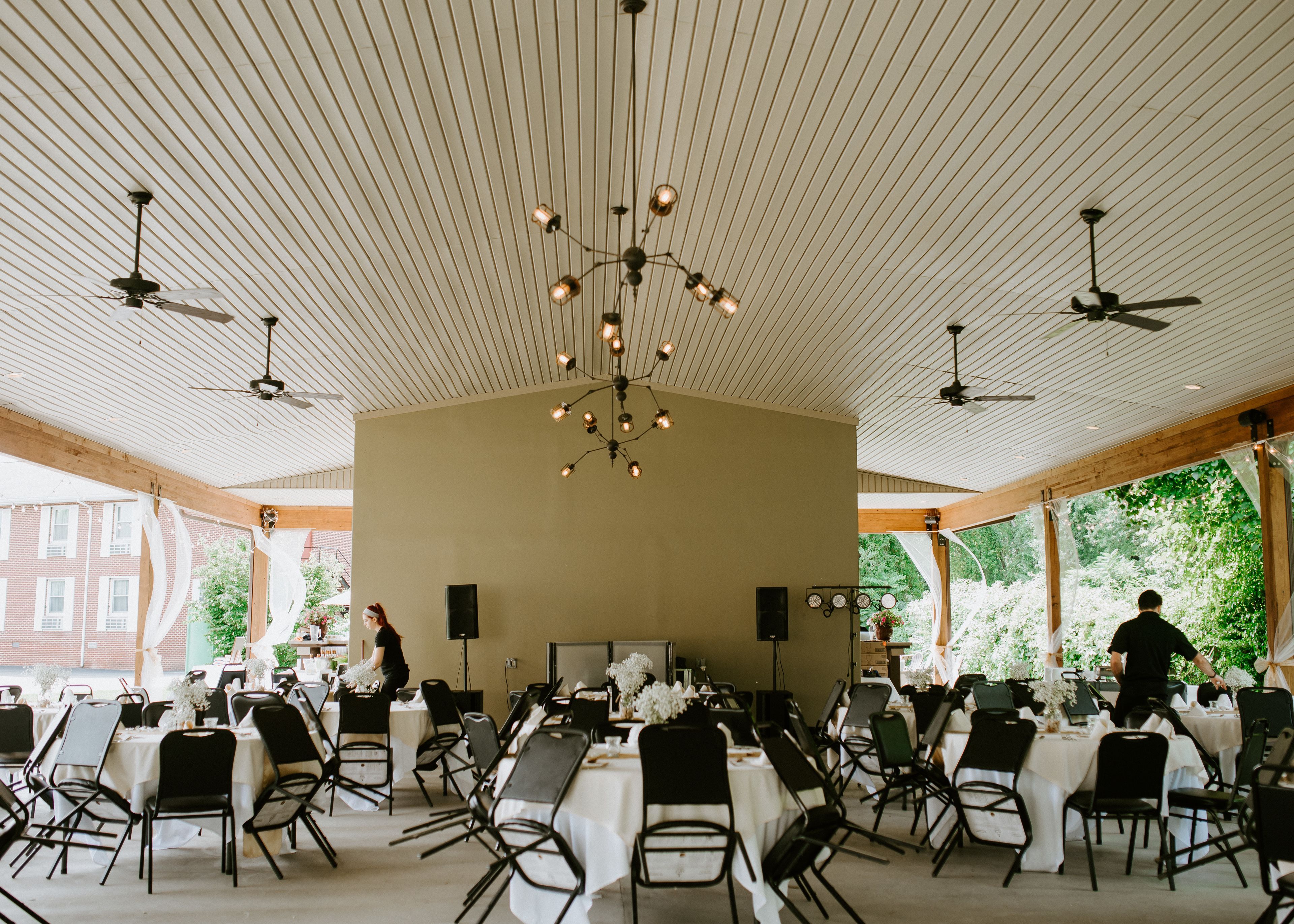 A spacious hall with high ceilings, multiple tables set for dining, and ceiling fans.