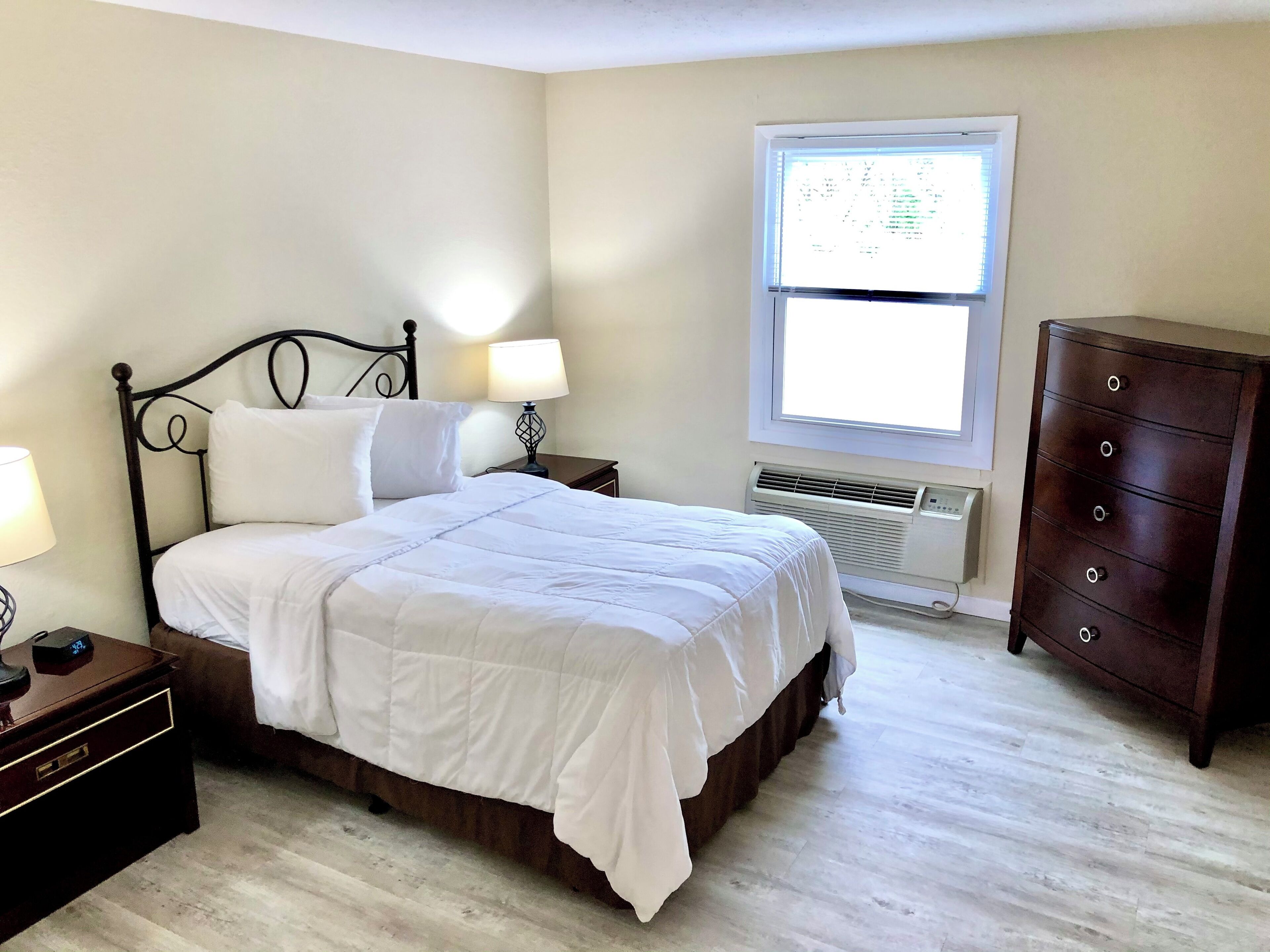 Un dormitorio ordenado con cama, mesitas de noche, cómoda y ventana con persianas.