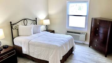 Un dormitorio ordenado con cama, mesitas de noche, cómoda y ventana con persianas.