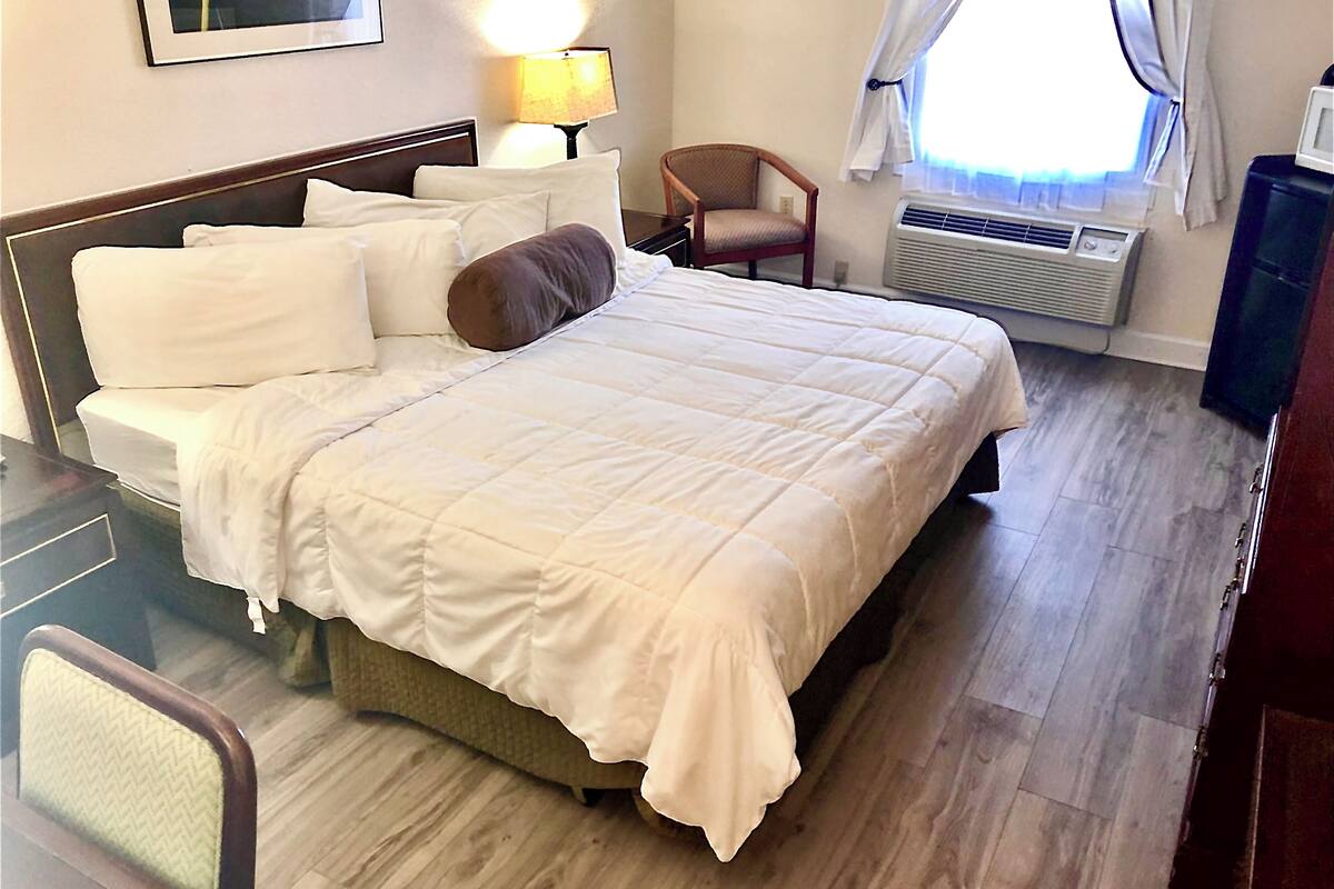 Une chambre d’hôtel avec un lit, une chaise, une lampe et une fenêtre avec des rideaux.