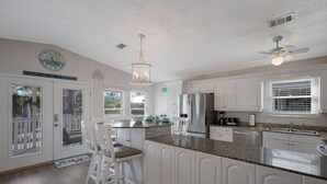 A kitchen with white cabinets, a stainless steel refrigerator, a granite countertop, and a ceiling fan.