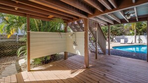 A wooden deck with a pool, surrounded by palm trees and a covered area with a staircase.