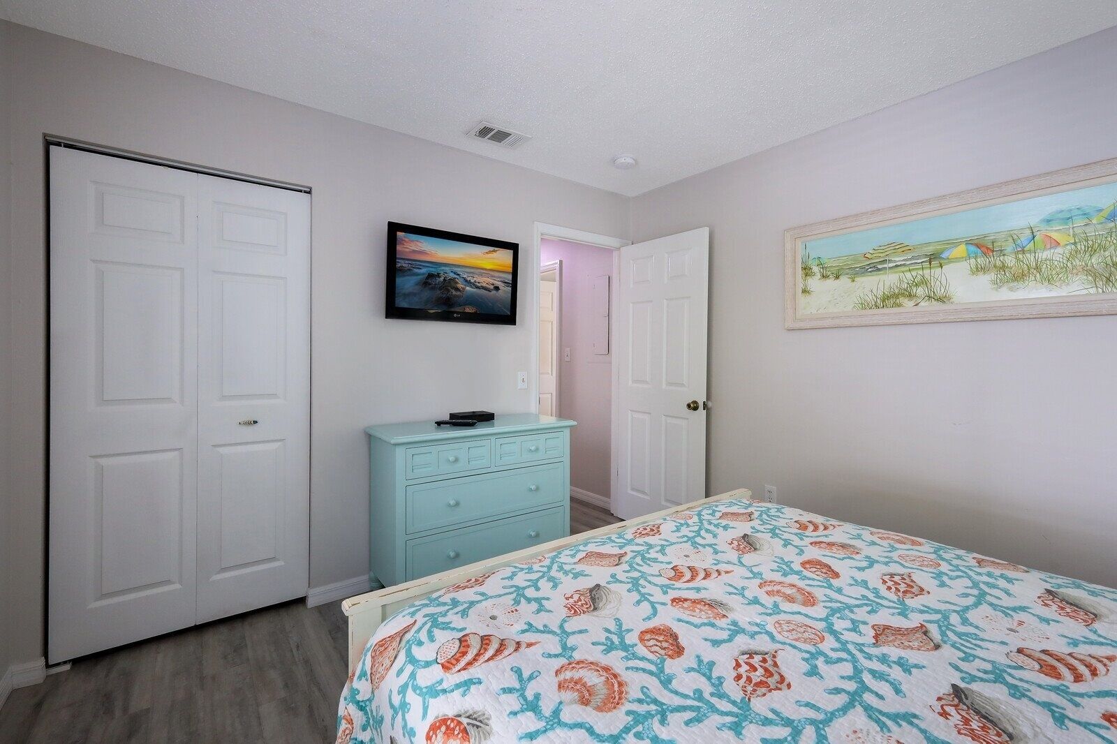 A bedroom with a bed, a dresser, a TV, and two doors.