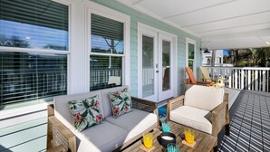 A covered porch with a white sofa, two chairs, and a small table with drinks.