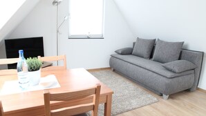 A modern living room with a wooden dining table, grey sofa, and a small potted plant. - Schwaben Apartment (Oberboihingen)