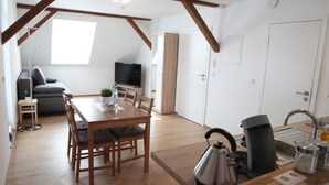 A modern kitchen with wooden flooring, a dining table with chairs, a kettle, a coffee maker, and a TV in the background. - Schwaben Apartment (Oberboihingen)