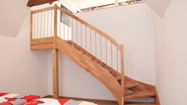 A bedroom with a wooden staircase, a bed with a red and white patterned bedspread, and a window with a view of the sky. - Schwaben Apartment (Oberboihingen)