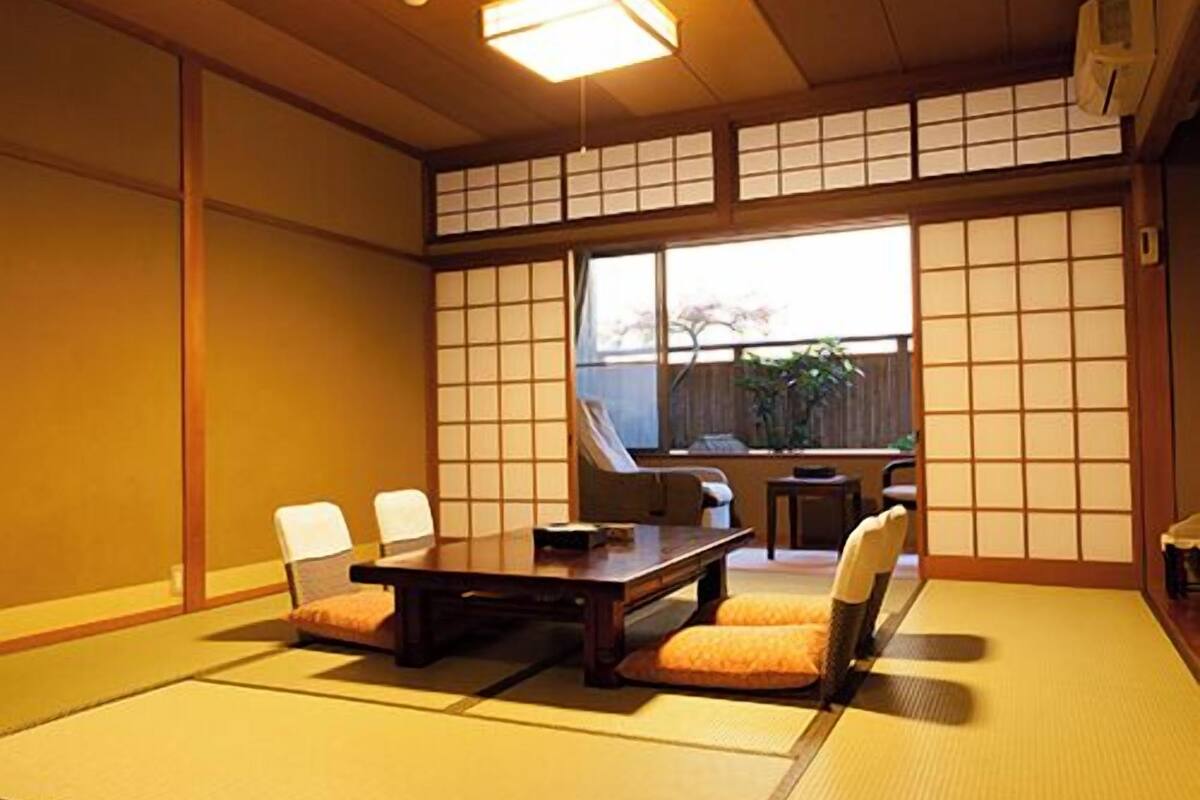 A tatami mat room with a low table and chairs, a window with a view, and a ceiling light.