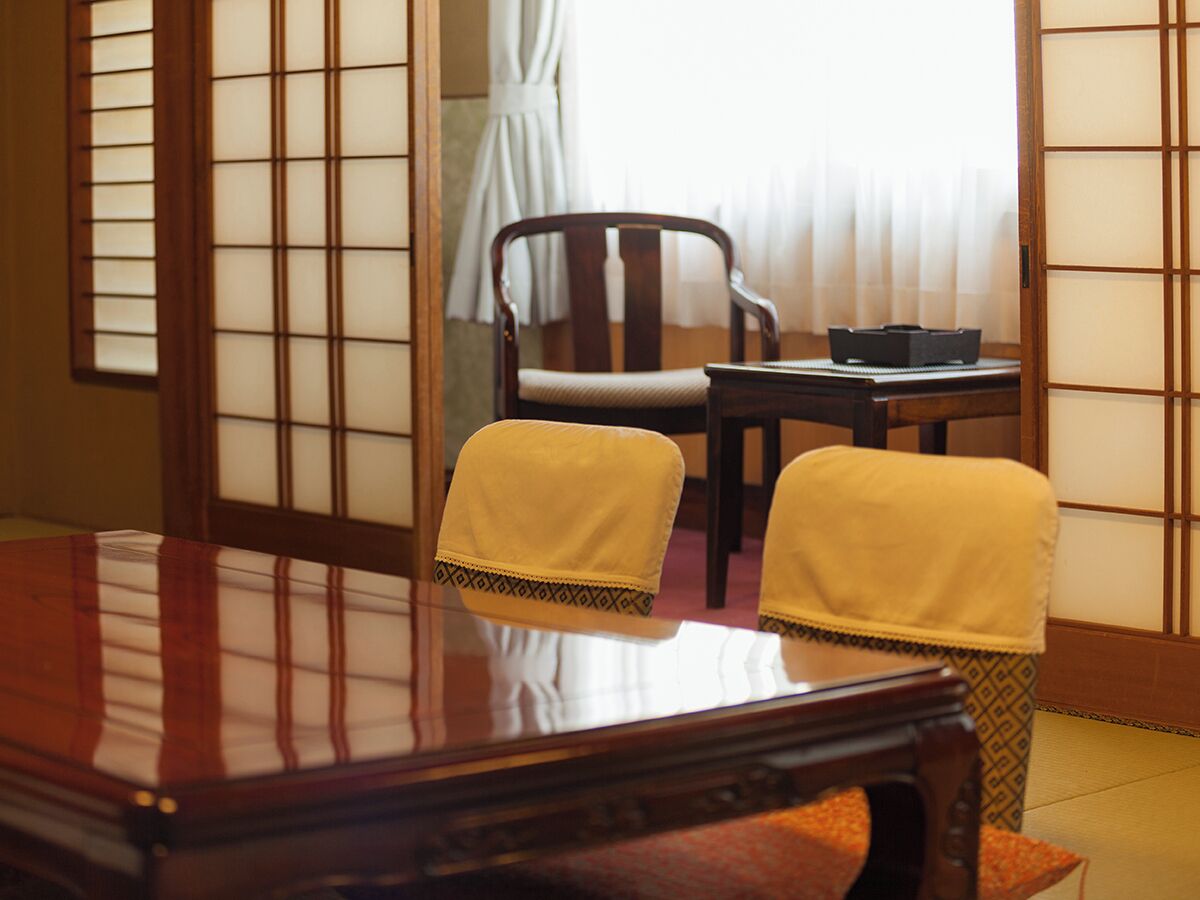 A traditional Japanese room with tatami flooring, a low wooden table, two chairs with cushions, and shoji screens.