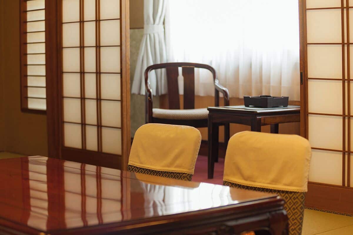 A traditional Japanese room with tatami flooring, a low wooden table, two chairs with cushions, and shoji screens.