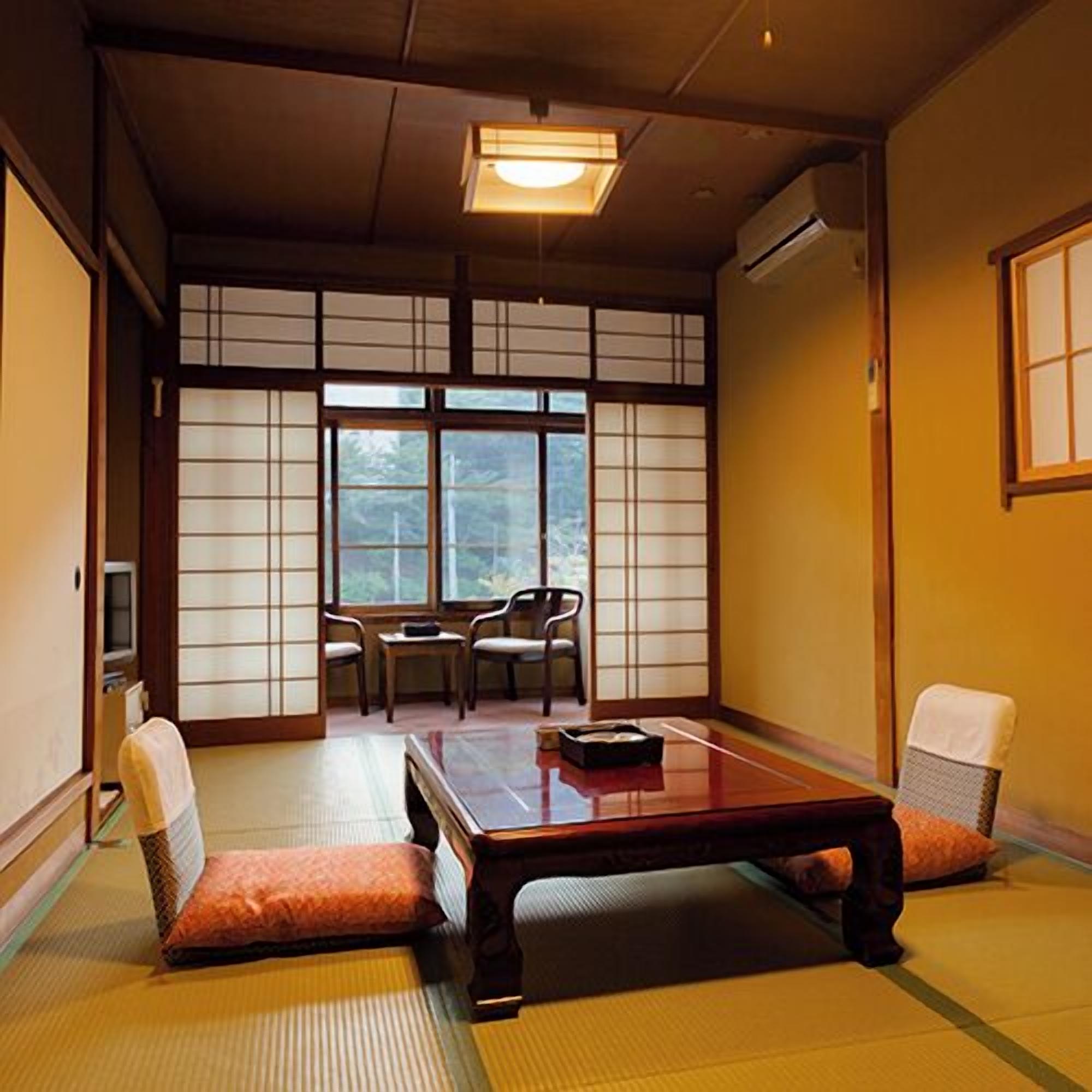 A traditional Japanese room with tatami flooring, a low table, two chairs, and a sliding shoji screen door.