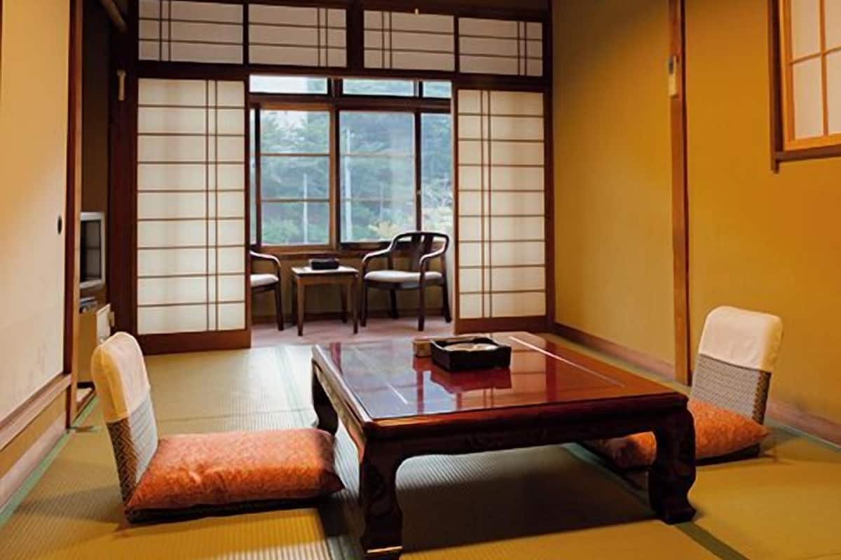 A traditional Japanese room with tatami flooring, a low table, two chairs, and a sliding shoji screen door.