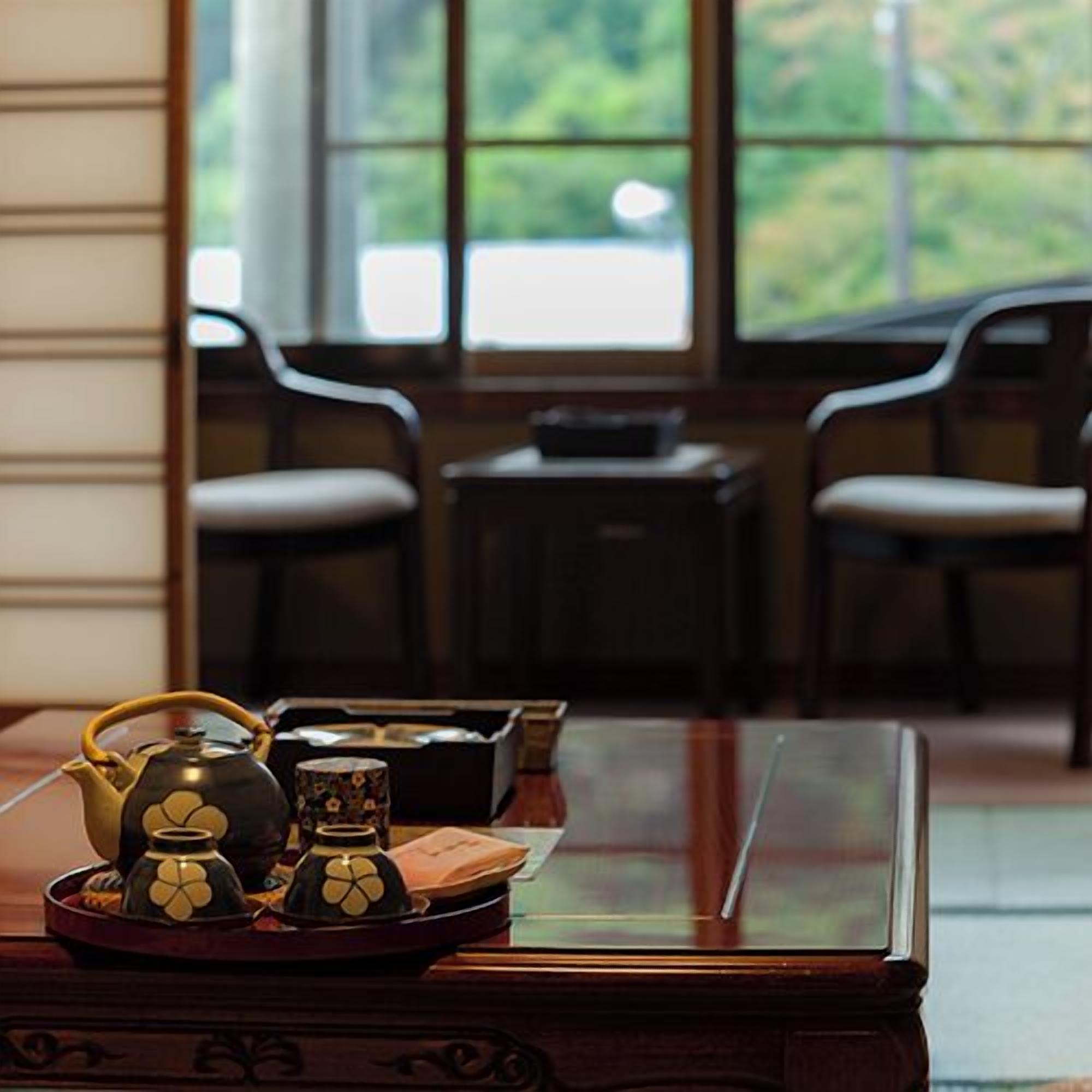 A room with a wooden table, a window with a view of greenery, and two chairs.