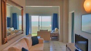 Ein Hotelzimmer mit großem Spiegel, einer Couch, einem Fernseher und einem Balkon mit Meerblick.