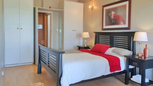 Ein ordentlich eingerichtetes Schlafzimmer mit Bett, Nachttischen, einem Kleiderschrank und einem gerahmten Bild an der Wand.