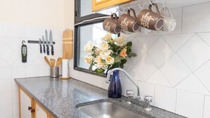 Eine Küche mit einer Granit-Arbeitsplatte, Spüle aus Edelstahl, hängenden Tassen, Messern und einer Vase mit Blumen.
