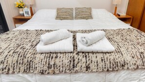 Ein ordentlich bezogenes Bett mit zwei Kissen, einer gemusterten Decke und zwei aufgerollten Handtüchern.